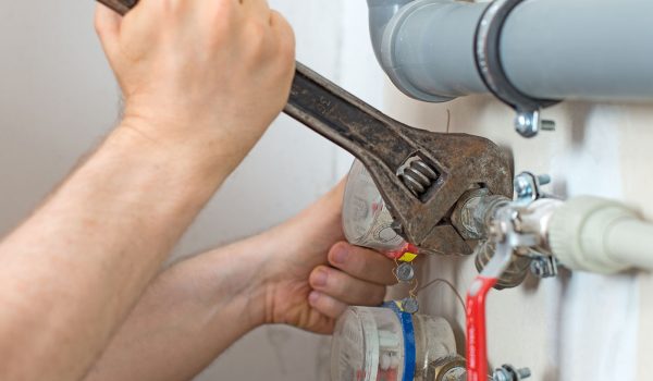 Male plumber fixing water meter with adjustable wrench.